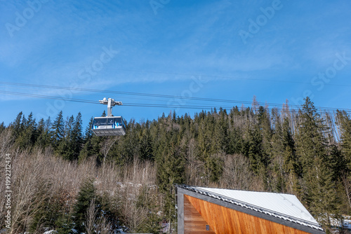 Cable car goes up the mountain in the clear blue sky near tall trees in wintertime. A cable car on the Kasprowy Wierch mountain. Zakopane, Poland