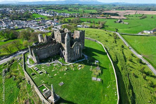 Aerial drone view of the Rock of Cashel, a historic medieval cathedral and fortress rising above the Irish countryside.