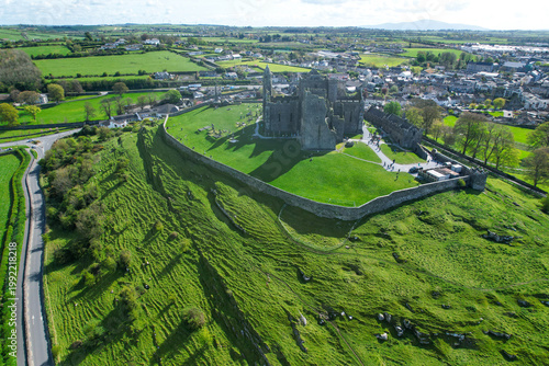 Aerial drone view of the Rock of Cashel, a historic medieval cathedral and fortress rising above the Irish countryside.