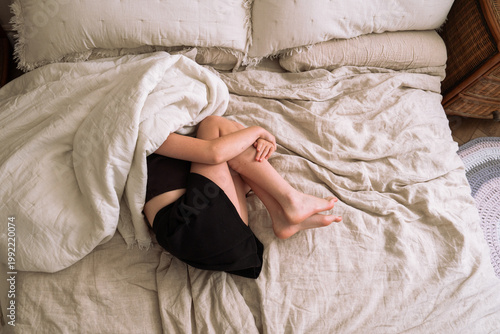 Relaxed girl lying in bed with a soft duvet partially covering her. Peaceful and cozy moment in a minimalist bedroom with natural linen bedding.