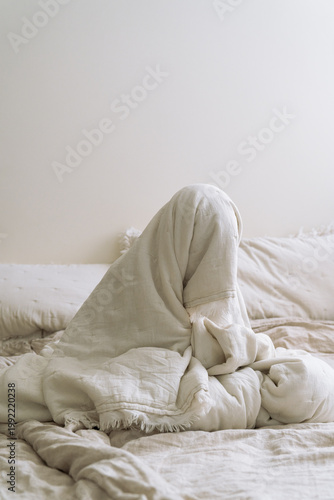 Woman or teenage girl wrapped in a linen blanket, sitting on a bed in a calm, minimalist bedroom. Soft light and cozy textures create a peaceful morning mood. beauty of slow mornings. Bed rotting