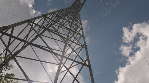 Low angle shot of a high voltage electricity transmission tower against a blue sky with clouds