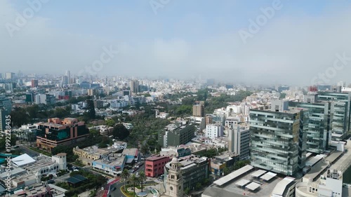 Cityscape Panorama in San Isidro, Peru: A wide aerial perspective captures a bustling urban landscape under a hazy sky, showcasing the architectural diversity and density of a modern city.