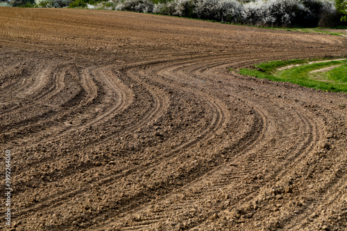 Freshly plowed agricultural field with curved tractor tracks and rich soil texture. Rural landscape in spring, ideal for farming, agriculture, and sustainability concepts
