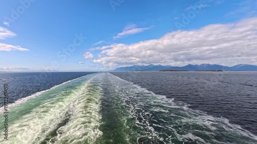 August 13, 2024 - Tracy Arm, USA - Cruise ship wake cutting through the water in Tracy Arm fjord in Alaska. Distant mountain range scenery underneath a partly cloudy sky.