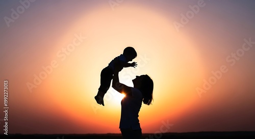 A mother joyfully throws her happy child up in the air against a breathtaking golden sunset sky creating a beautiful silhouette