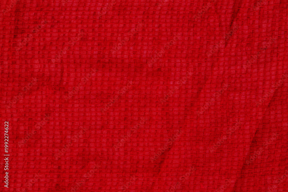 Fototapeta premium Bright red fabric with a textured surface on display in a bright light setting, possibly indoors or outdoors