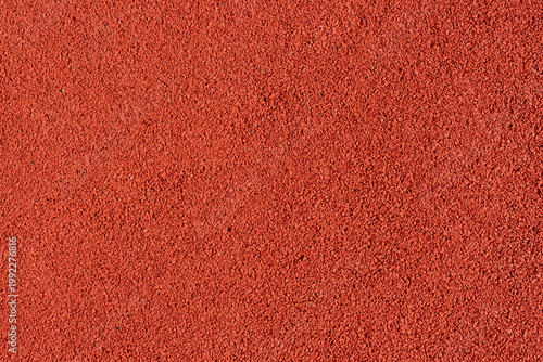 Red rubber crumb playground or sports surface texture, captured full frame as a bright granular background for design use. Abstract red textured background.