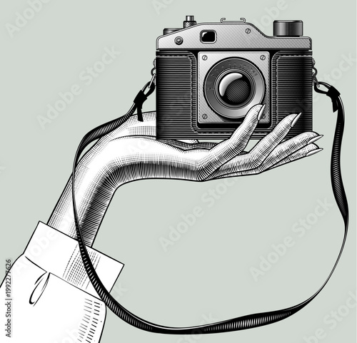 Palm of the hand with a vintage camera in front view. Detailed line art with cross-hatching shows lens, knobs, viewfinder and straps. vector illustration in 
black and white engraving style. 
