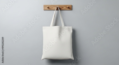 Blank white tote bag hanging on a wooden hook against a gray wall background.