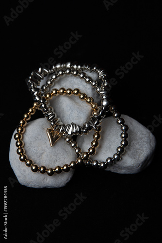 Stylish beaded bracelets in gold and silver tones on white stones, minimalist black backdrop