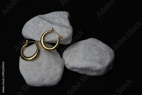 White stones cradle gold hoop earrings, bold black background, elegant jewelry composition