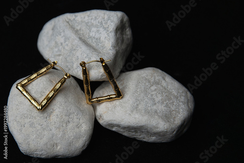 Geometric gold hoop earrings on white stones, stark black background — modern jewelry showcase
