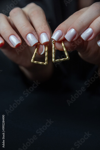 Fashionable gold square earrings in close-up, manicured hands add elegance to the shot