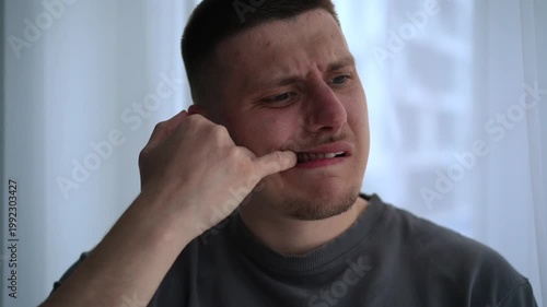 Close-up of a young man opening his mouth and checking between his teeth with his fingers in a bright room. His calm but slightly uneasy expression suggests minor irritation rather than pain.