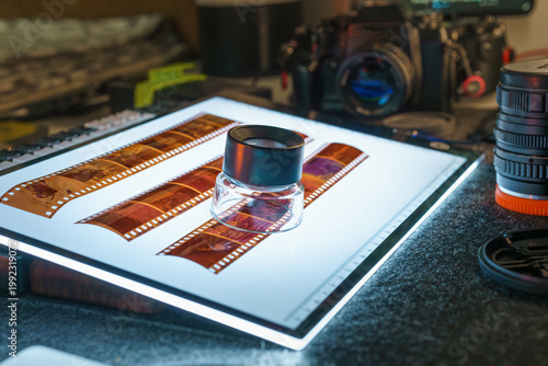 Photographer hand using magnifying loupe 35mm film strips light table