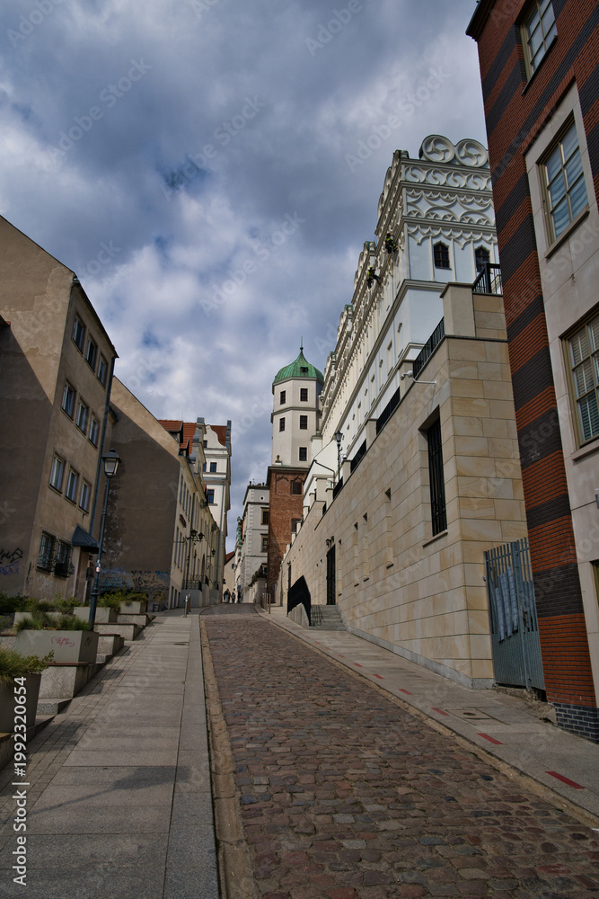 Fototapeta premium Historic European Cobblestone Street Lined With Ornate Buildings And Tower Under Dramatic Sky - Szczecin - Castle of the Pomeranian Dukes.
