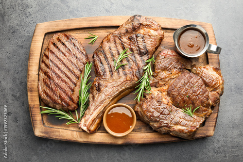 Schilderij op canvas Grilled beef steaks with sauce and rosemary on grey table, top view