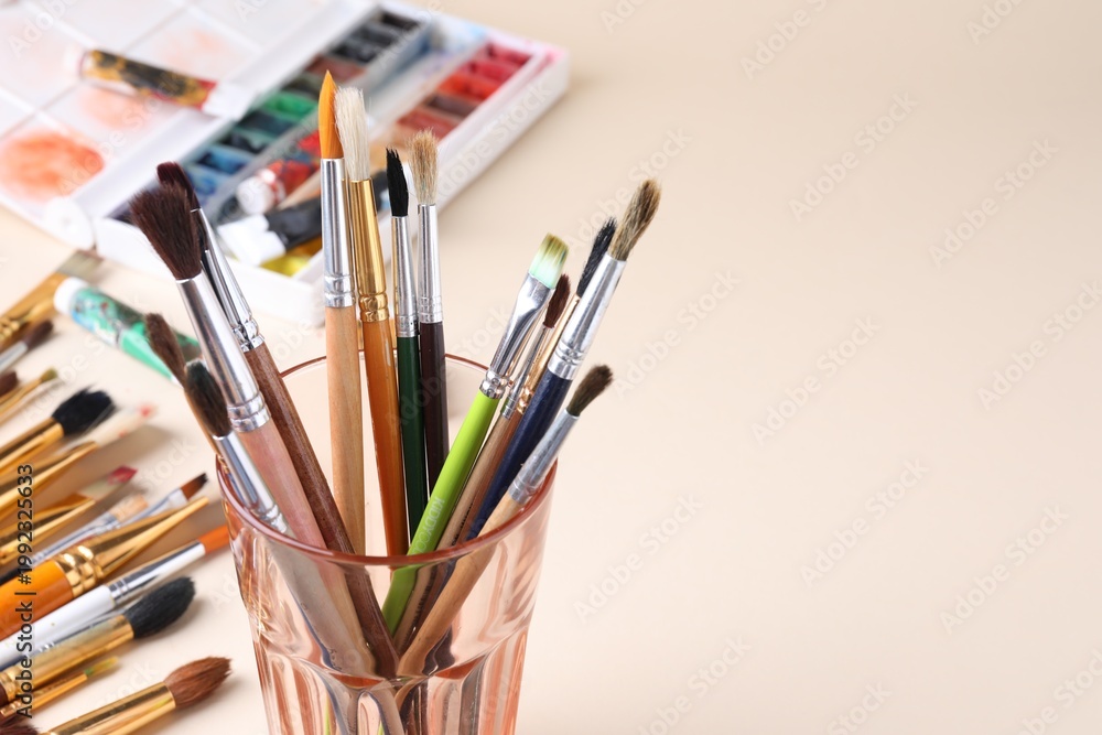 Obraz premium Paintbrushes in glass and paints on beige background, closeup. Space for text