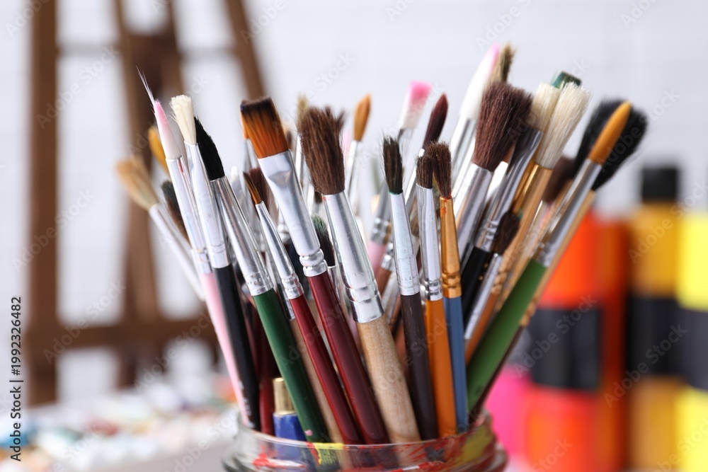 Fototapeta premium Different paintbrushes in holder on blurred background, closeup