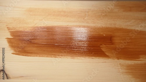 Hand brushing dark stain across wooden board during indoor renovation work.