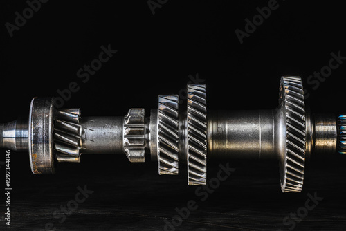 Worn gearbox shaft with cracks, pitting, scratches, and discoloration, in a dark industrial space with focus on gear wheels, symbolizing time, pressure and heavy load operation