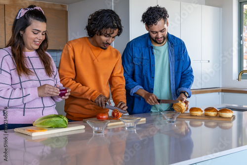 Diverse friends prepping at glossy kitchen island, slicing tomato on wooden cutting boards