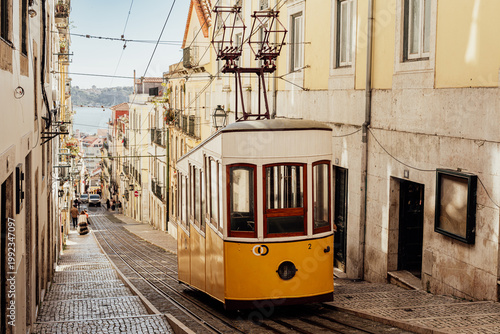 Historic yellow tram on steep Lisboa street in warm photography style on sunny urban backdrop, concept of travel and culture