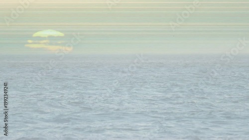 Ocean surface dominating, rolling and breaking with foam while sun brightening, revealing horizon