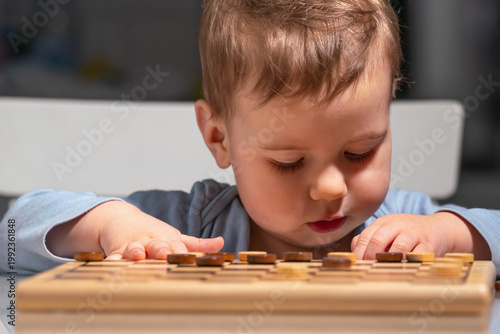 Cute toddler playing checkers, learning through simple board game at home.