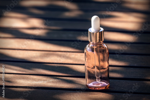 Glass dropper bottle mockup with cosmetic oil on wooden table in natural light with soft background and copy space