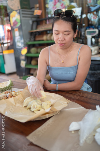 Woman Enjoying Durian at a Vibrant Market Buffet with Refreshing Drink