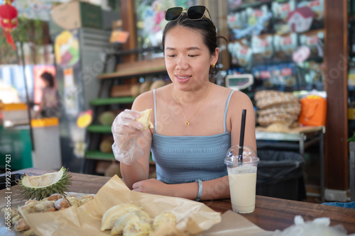 Asian Woman Enjoying Durian at a Vibrant Market Buffet with Refreshing Drink