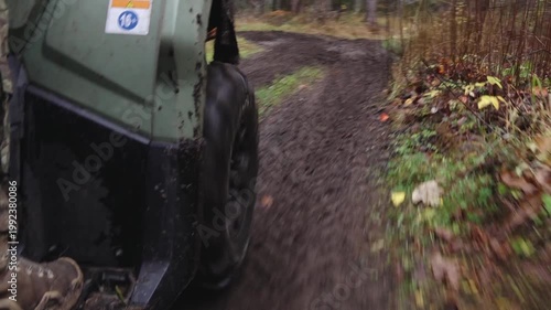 Six-wheeled ATV navigating a muddy trail through a forest, showcasing tire movement and dirt splatter in a natural setting