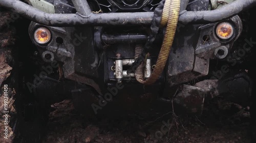 Six-wheeled ATV front view with visible winch and lights, showcasing rugged design and muddy terrain in outdoor environment