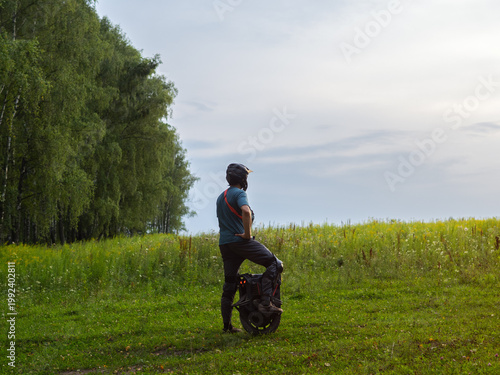 A man on an electric mono wheel poses in a green field. Eco-friendly modern individual transport