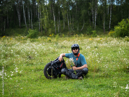 young man poses in nature next to a mono wheel. Modern eco-friendly transport.