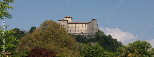 Vászonkép Angera, Italy - April 20, 2026: Rocca di Angera, historic medieval fortress overlooking Lake Maggiore in Lombardy, Italy, surrounded by lush green trees under clear blue sky