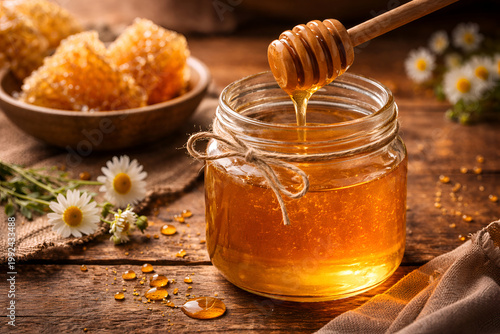 Honey dripping from wooden dipper into glass jar with honeycomb and chamomile flowers on rustic table, natural organic sweetness and healthy food concept