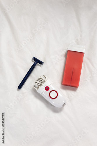Red wax cartridge with wooden spatulas vs epilator vs razor. Compact devices arranged for DIY home wax depilation prep. Clean minimal styling. concept of choosing between hair removal products