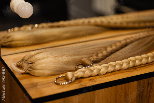 Close up of blonde braid extensions with metal rings on wooden table, front view. Concept hair extensions, beauty products, natural tones, hairstyling materials, salon workspace.