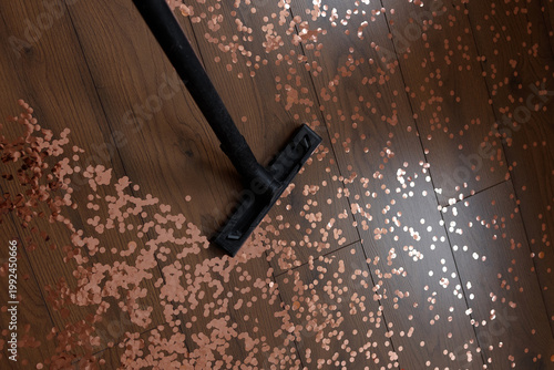 Vacuum cleaner nozzle on wooden floor with pink confetti scattered around, top view. Concept of cleaning after party, mess, household chores, celebration cleanup.