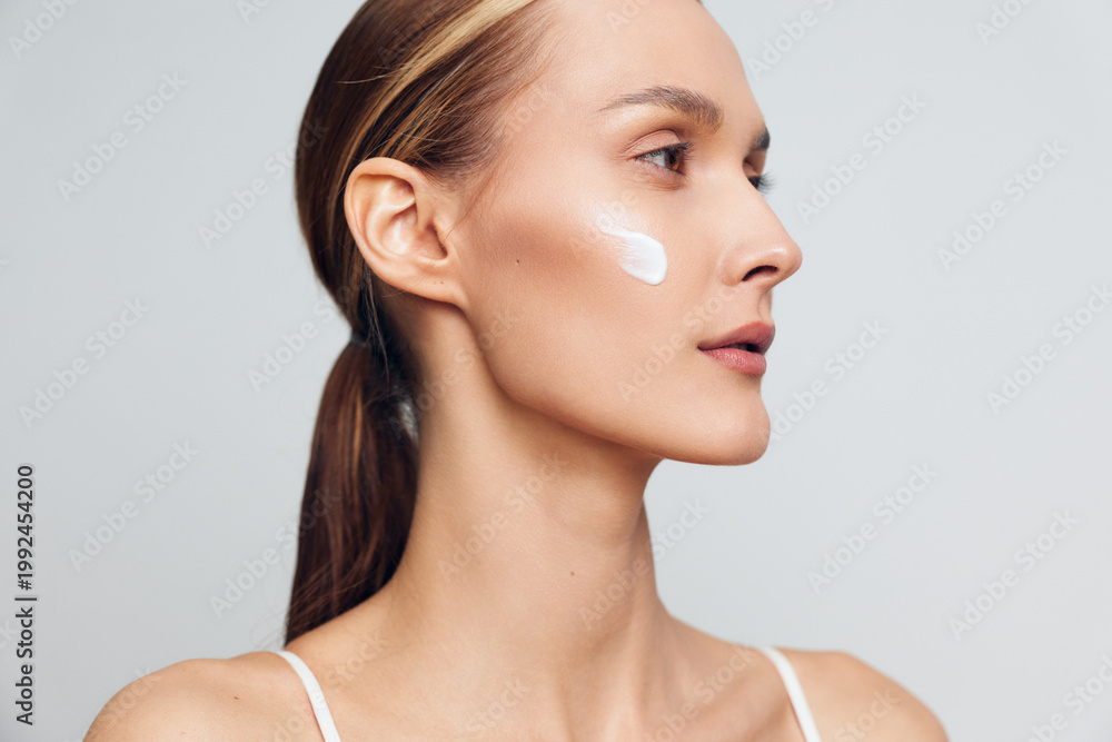 Obraz premium Woman applying face cream, skincare self care close up profile on a light gray background, soft studio lighting, smooth skin care concept, calm mood beauty routine