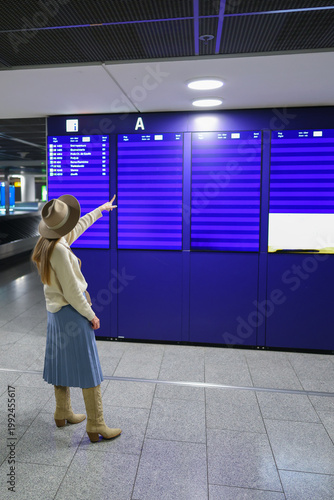 Woman in hat at airport board, waiting and planning next trip concept.