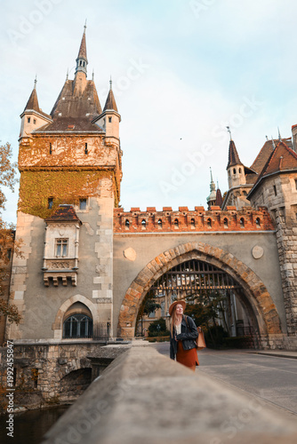 Smiling woman in hat at medieval castle archway, popular tourist attraction in Europe.