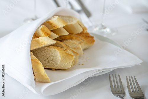 Slices of fresh baguette wrapped in a white napkin on an elegant table for a festive dinner, concept for holiday events like Wedding, Christmas, anniversary or a similar occasion, selected focus
