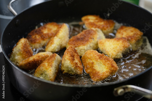 Frying breaded pieces of meat or fish in hot oil in a black pan, they become extra crispy thanks to Japanese panko breadcrumbs, selected focus