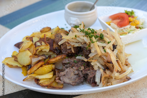 Pan-fried chicken liver with fried potatoes and onions, served with a side salad and a bowl of mashed apples on a plate at a casual dining restaurant in Germany, selected focus