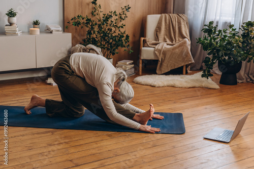 Fotografija Senior woman sits on yoga mat twisting torso with straight spine