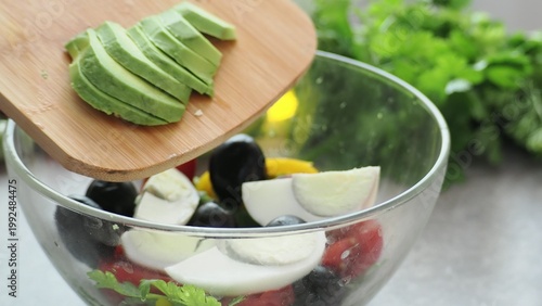 A girl prepares a delicious, low-calorie, and healthy salad. Keto diet. Balanced protein and fat, high in fiber. Salad with avocado, greens, bell pepper, egg, olives, parsley, and dill, tomatoes